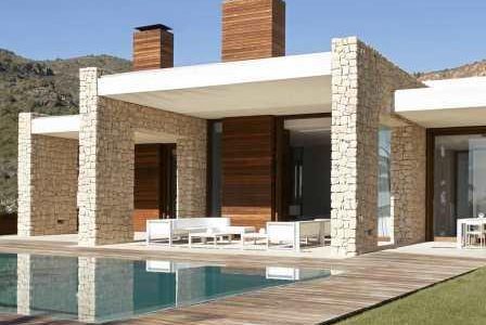 Construção de moradia com fachada revestida a pedra e deck de madeira a envolver piscina.
